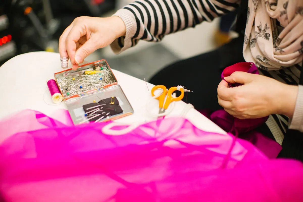 Seamstress hand-pinning fabric with a thimble, scissors and thread beside her