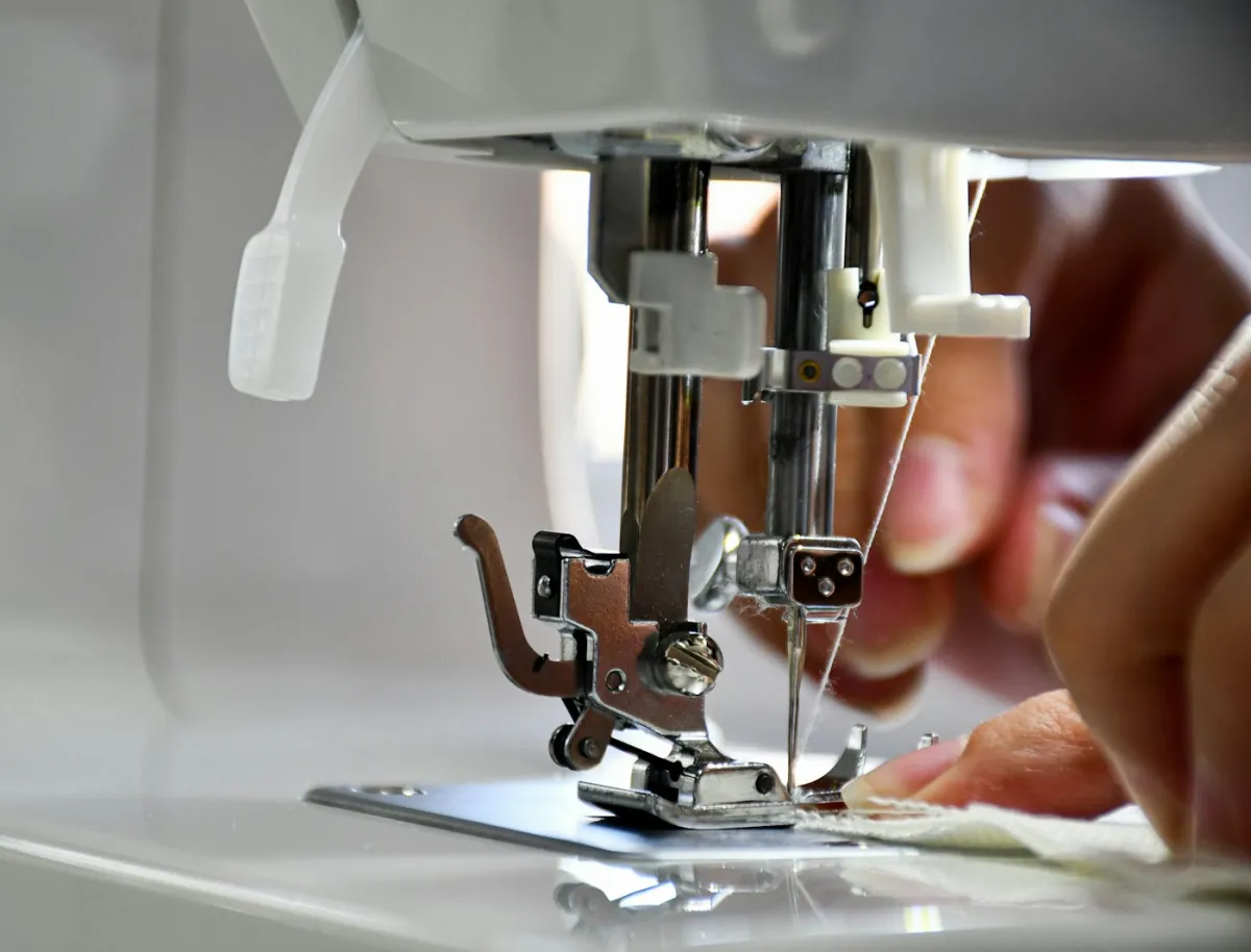 Seamstress guiding fabric under a sewing machine needle in a bright studio